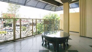 A balcony with a glass table and chairs, a metal railing, and a view of the street below. - RedDoorz Syariah @ Jalan Gajah Mada (Jember)