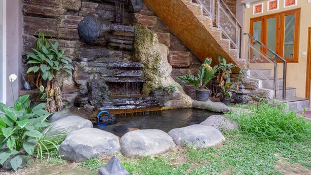 Un muro de piedra con una fuente, plantas en macetas y una escalera.