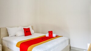 Una cama bien hecha con una colcha roja y amarilla, almohadas blancas y una almohada roja con un logotipo.