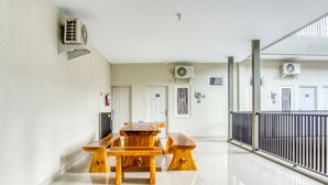 Una habitación amplia con una mesa de madera y bancos, unidades de aire acondicionado en las paredes y un balcón con baranda de metal.
