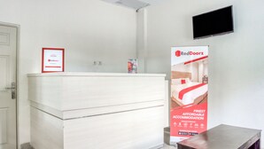 Un mostrador de recepción con un diploma enmarcado, un anuncio de RedDoorz y un televisor montado en la pared.