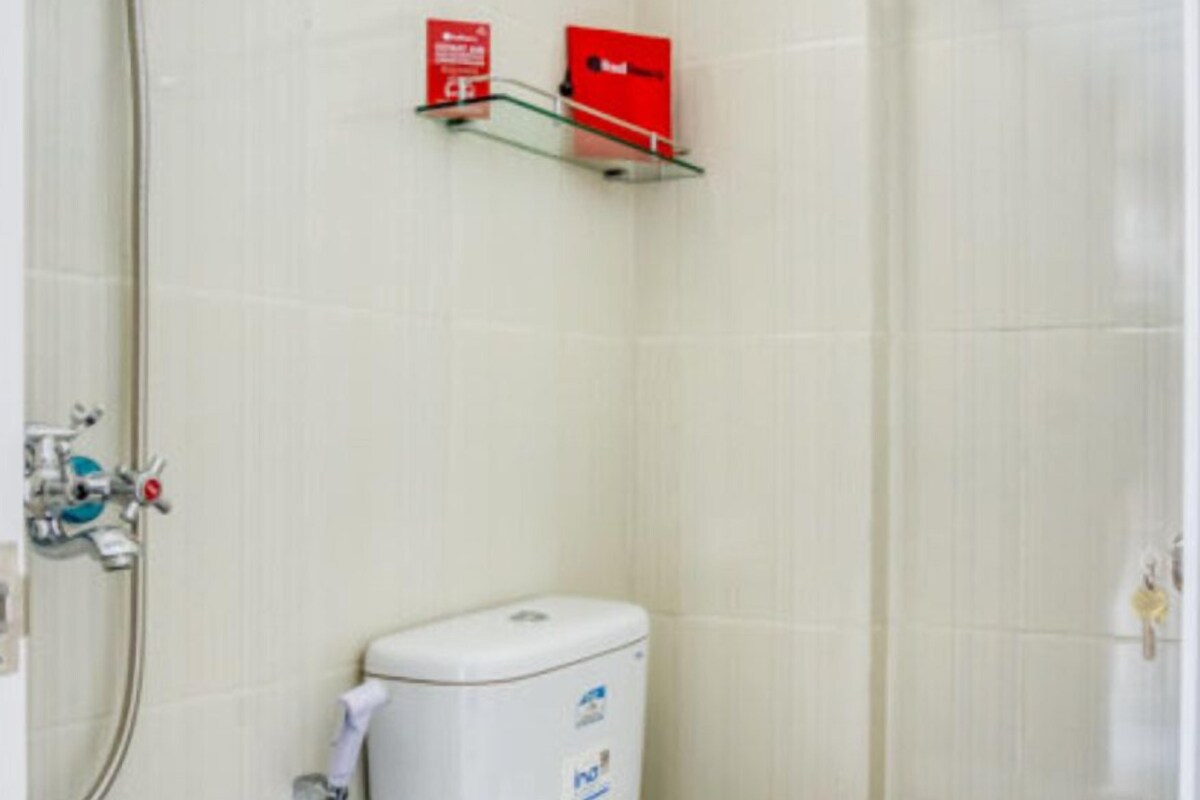 Un baño con inodoro, un estante de vidrio con una caja roja y una zona de ducha.