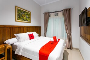 A hotel room with a wooden headboard, a bed with white bedding and a red accent, a painting on the wall, and a window with curtains. - RedDoorz Near Universitas Muhammadiyah Yogyakarta (Kasihan)
