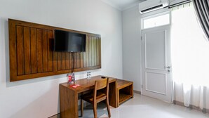 Una habitación con un escritorio de madera, una silla, un televisor de pantalla plana montado en un panel de madera y una puerta blanca con un ventanal.