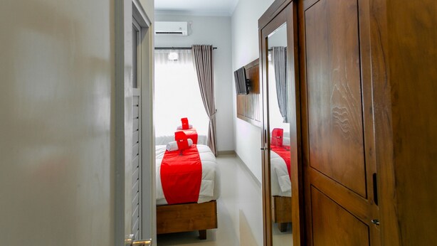 Una habitación de hotel con un armario de madera, una cama con colcha roja y una ventana con cortinas.