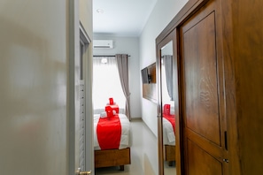A hotel room with a wooden wardrobe, a bed with a red bedspread, and a window with curtains. - RedDoorz Near Universitas Muhammadiyah Yogyakarta (Kasihan)