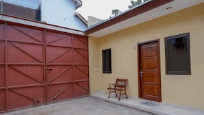 A building with a red metal gate, a wooden door labeled "V1", and a bench outside. - RedDoorz near Living Plaza Purwokerto (Purwokerto)