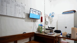 A small office with a wooden bench, a desk with a computer, and a wall-mounted TV displaying a calendar. - RedDoorz near Living Plaza Purwokerto (Purwokerto)