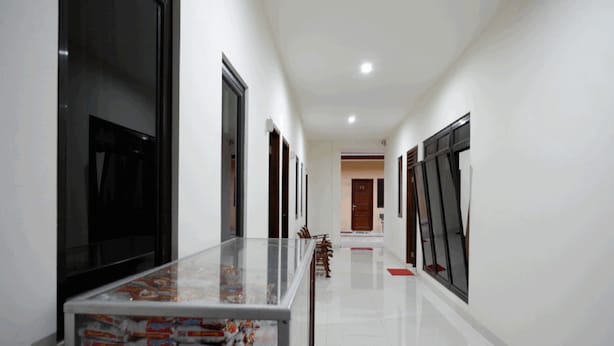 A hallway with a glass-top table displaying snack packages, wooden chairs, and a red mat on the floor. - RedDoorz near Living Plaza Purwokerto (Purwokerto)