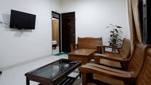 A living room with a flat-screen TV mounted on the wall, a wooden coffee table, and two wooden chairs. - RedDoorz near Living Plaza Purwokerto (Purwokerto)