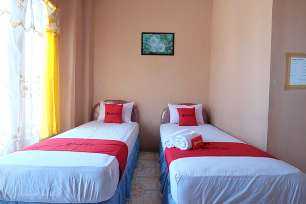 Ein Hotelzimmer mit zwei Einzelbetten, jedes mit einem roten Kopfkissen und einer weißen Bettdecke. Darüber an der Wand hängt ein gerahmtes Bild.
