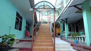 A staircase leading to a second floor with a metal railing, surrounded by a turquoise building with a tiled floor and steps.