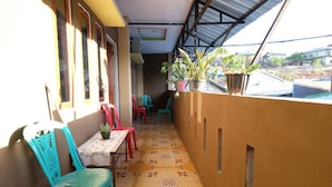 A covered balcony with a tiled floor, potted plants, and plastic chairs.