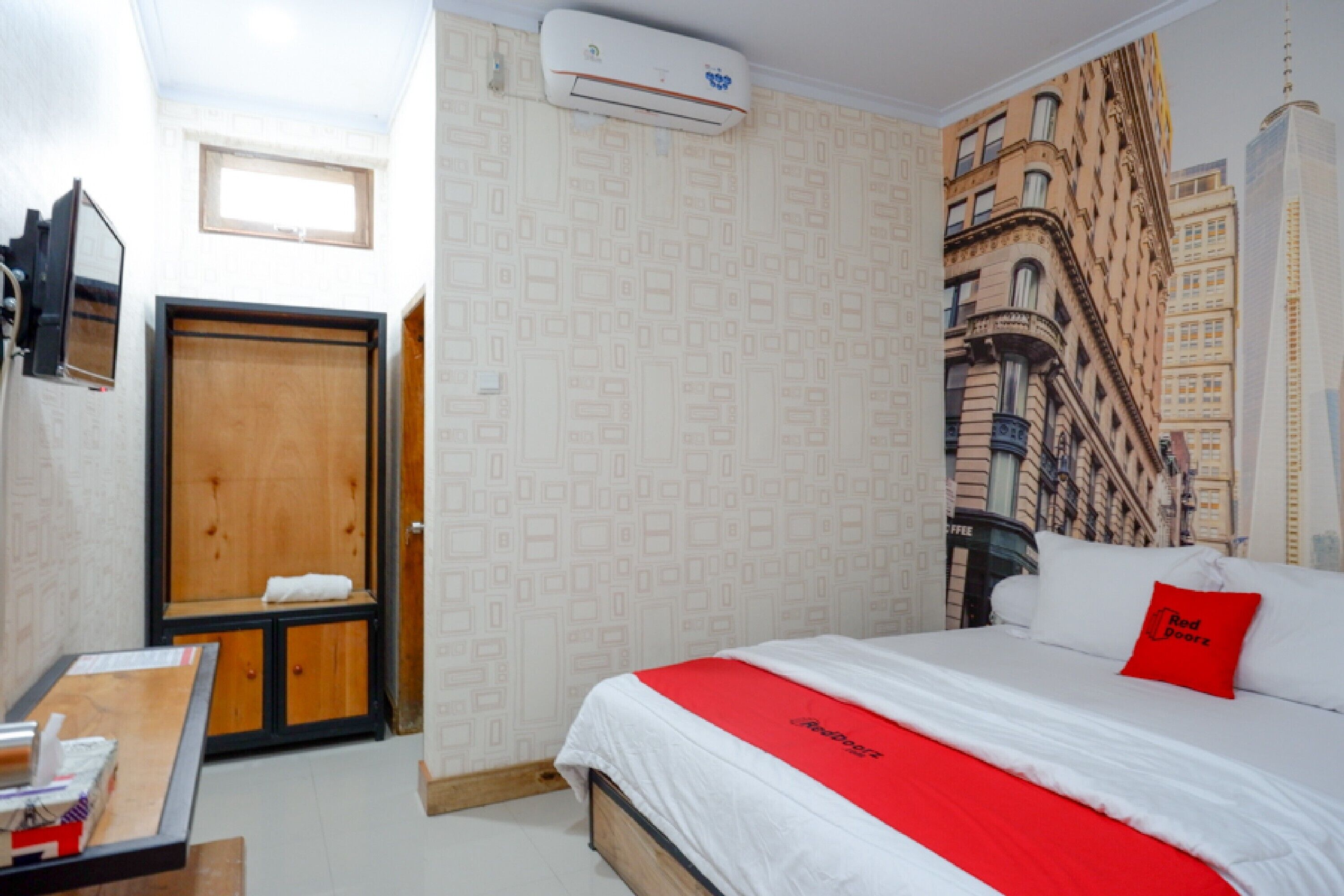 Une chambre d’hôtel comprenant un lit, une armoire en bois, un bureau et un climatiseur fixé au mur.