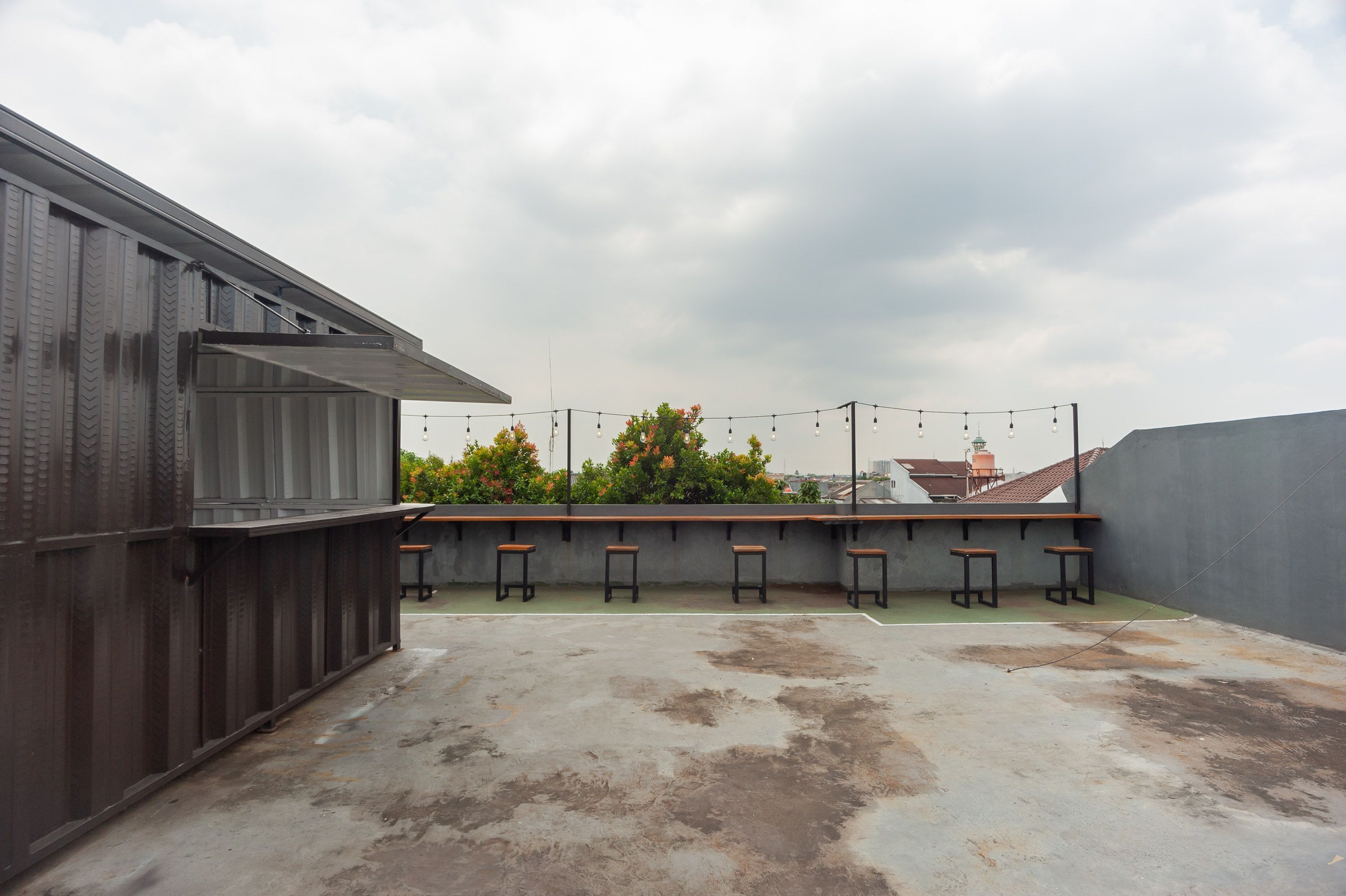 Una terraza en la azotea con piso de concreto, barandillas de metal y una fila de taburetes de madera.