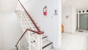 Escada com grades brancas e degraus pretos, um extintor fixado na parede e uma placa indicando a direção de um café.