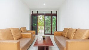 Quarto com dois sofás de couro, uma mesa de centro de madeira e uma porta de vidro que dá para uma varanda com vista para árvores.