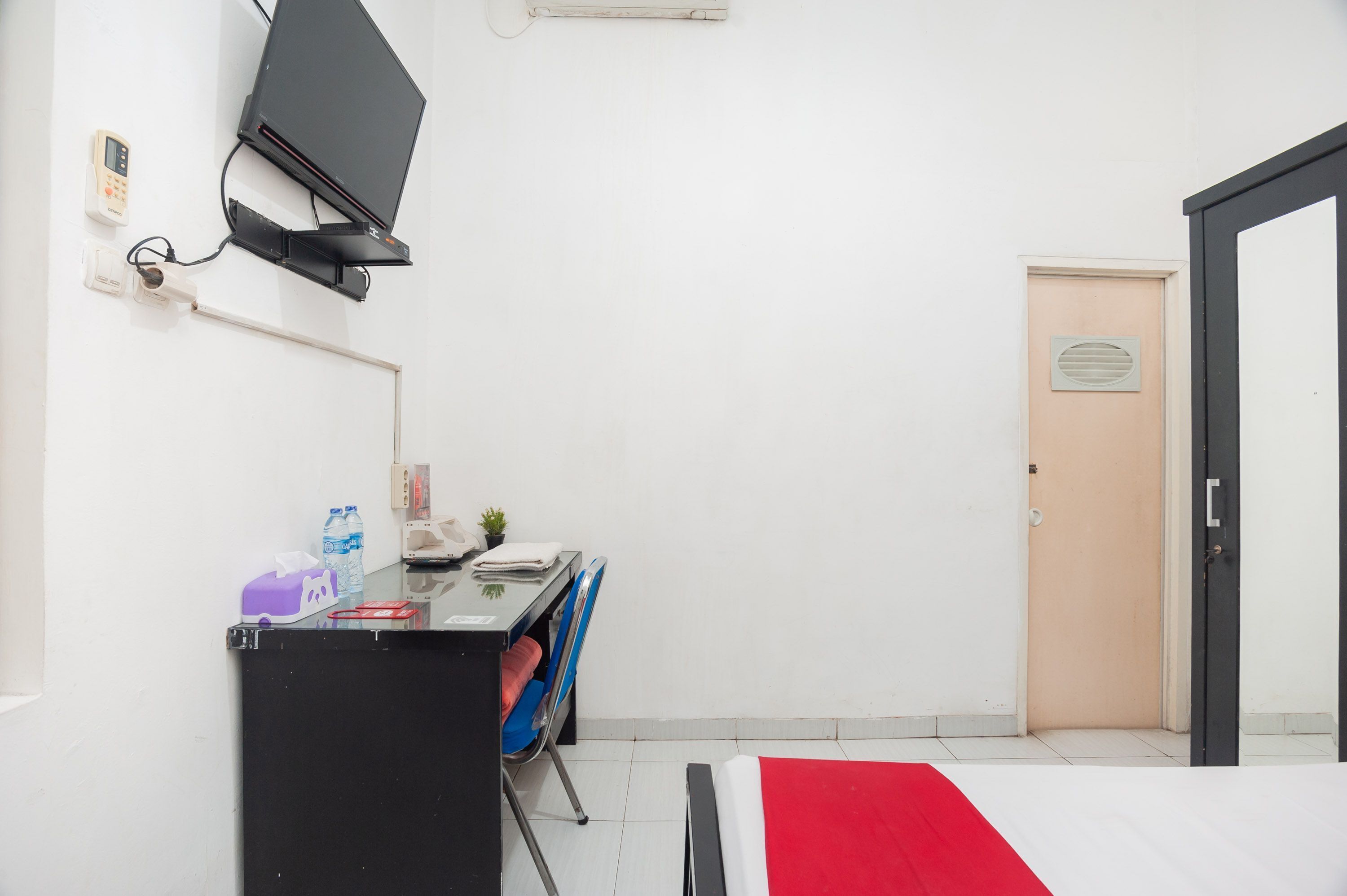 A small, clean room with a bed, a desk with a computer and a monitor, a door, and a window.