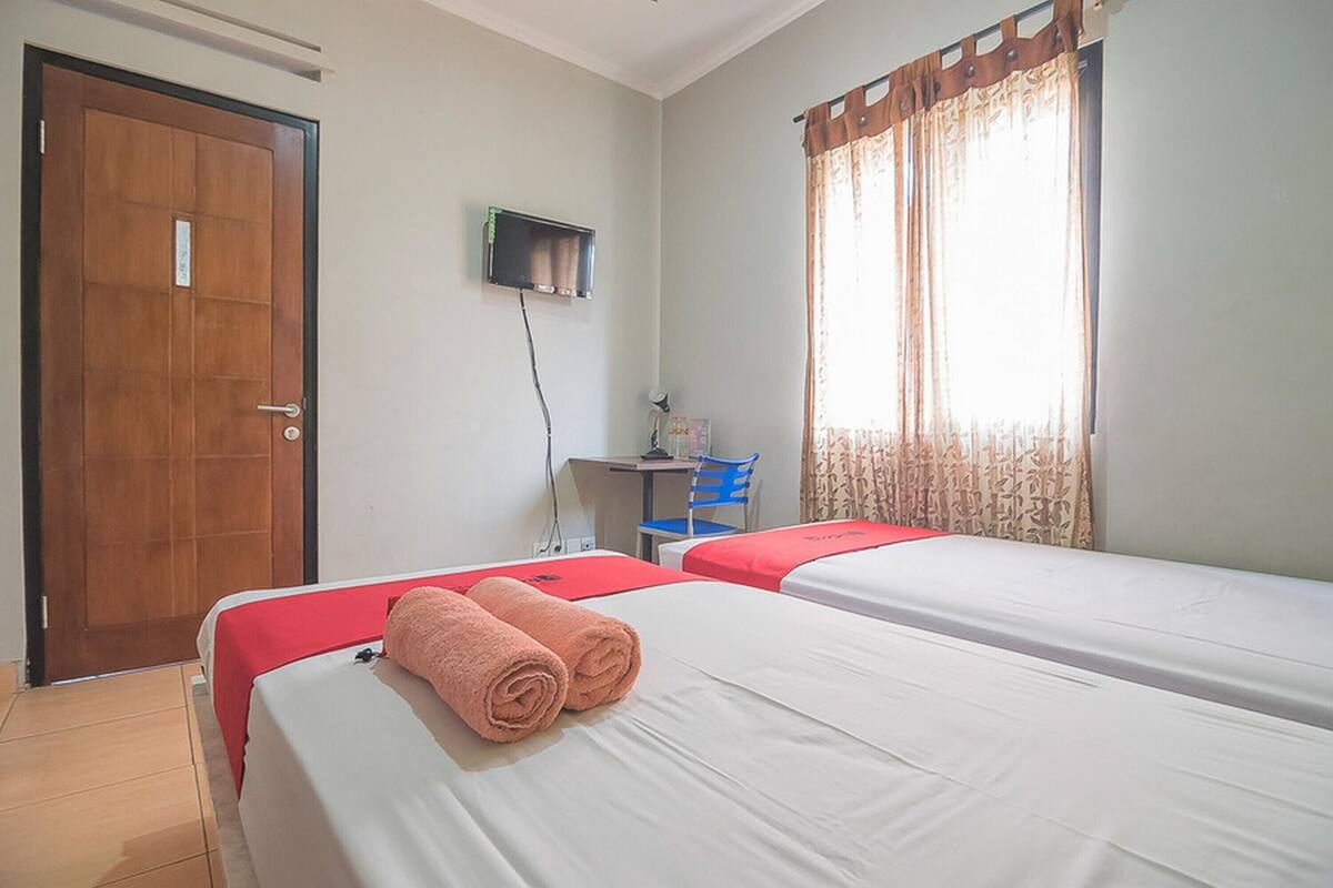 A hotel room with two beds, a desk, a chair, and a TV.