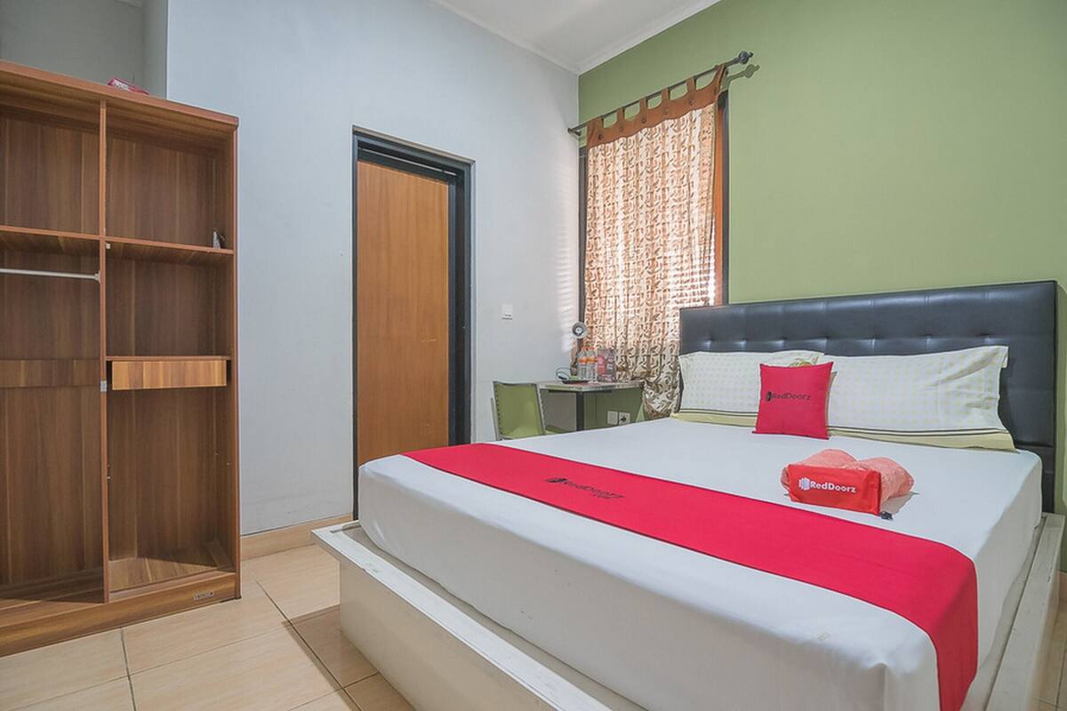 A bedroom with a bed, a wardrobe, a desk, and a window with curtains.
