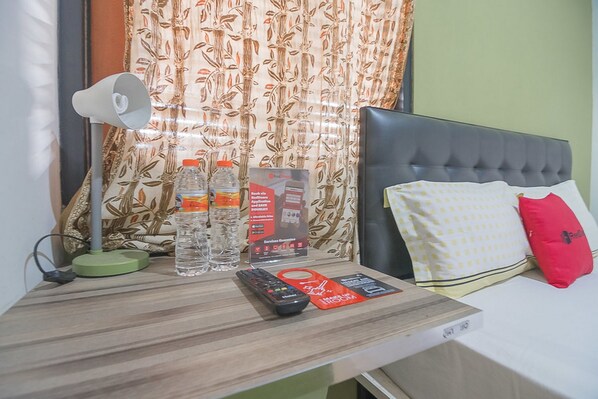 Habitación de hotel ordenada con cama, mesita de noche, lámpara, control remoto y un juego de botellas de agua.