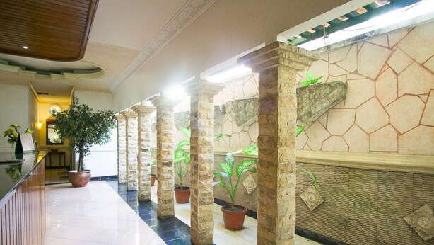 Un couloir orné de colonnes en pierre, de plantes en pot et doté d’un sol carrelé.