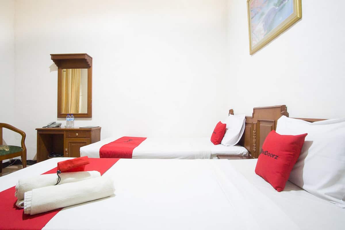Quarto de hotel com duas camas, uma escrivaninha de madeira, uma cadeira e um espelho.