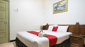 Un lit bien fait, recouvert d’une couvre-lit blanche et rouge, avec une tête de lit en bois et une table de chevet sur laquelle se trouve une lampe.