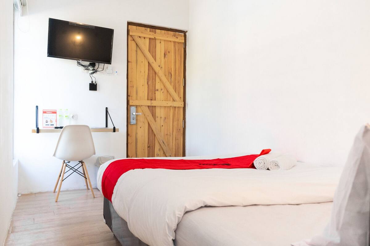 A bedroom with a bed, a TV mounted on the wall, a wooden door, and a chair.