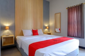 Ein Hotelzimmer mit einem großen Bett, zwei Nachttischen mit Lampen, einem Holz-Kopfteil, einem Spiegel und einem Fenster mit Vorhängen.