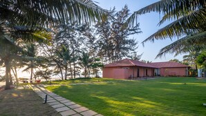 A red building with a tiled roof, surrounded by a well-maintained lawn and palm trees. - Regenta Place Mandrem Beach-Resort (Mandrem)