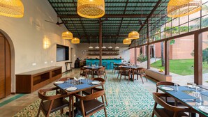 A restaurant with wooden tables and chairs, hanging wicker lamps, and a patterned floor. - Regenta Place Mandrem Beach-Resort (Mandrem)