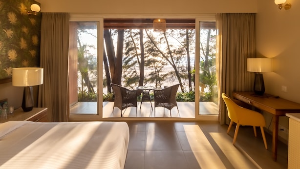A hotel room with a large bed, a desk, a chair, and a view of the outdoors. - Regenta Place Mandrem Beach-Resort (Mandrem)