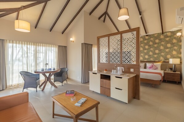 A hotel room with a dining area, a bed, a desk, and a large window with curtains. - Regenta Place Mandrem Beach-Resort (Mandrem)