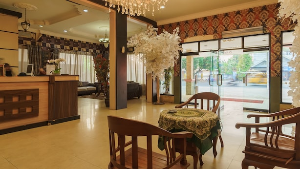 Een hotellobby met een receptiebalie, een kroonluchter, een eetgedeelte met een tafel en stoelen, en een groot raam met uitzicht op het omliggende landschap.
