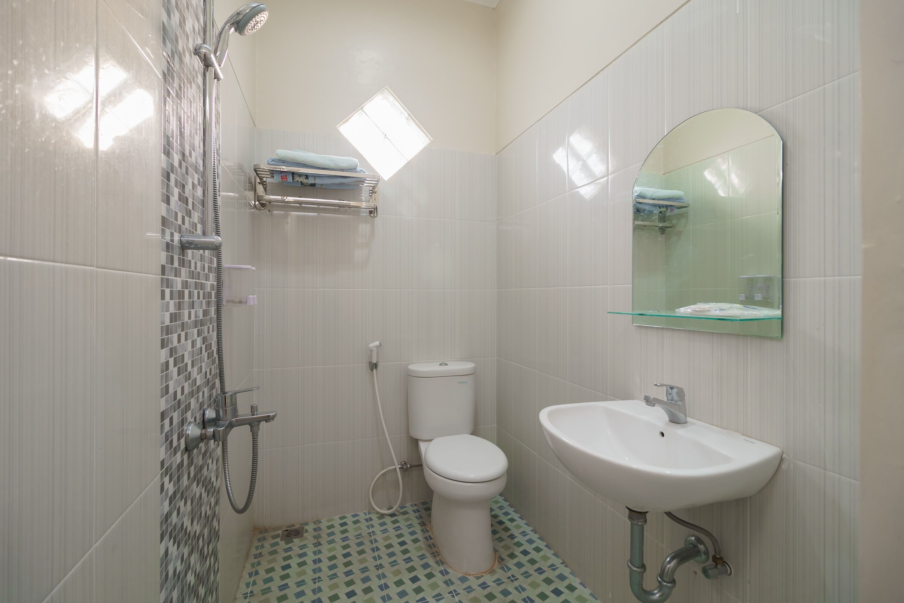 Un baño con ducha, inodoro, lavamanos y un estante pequeño con toallas.