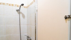 A bathroom with white tiled walls, a shower with a handheld showerhead, and a door with a simple latch mechanism. - RedDoorz @ Kebon Kacang (Jakarta)