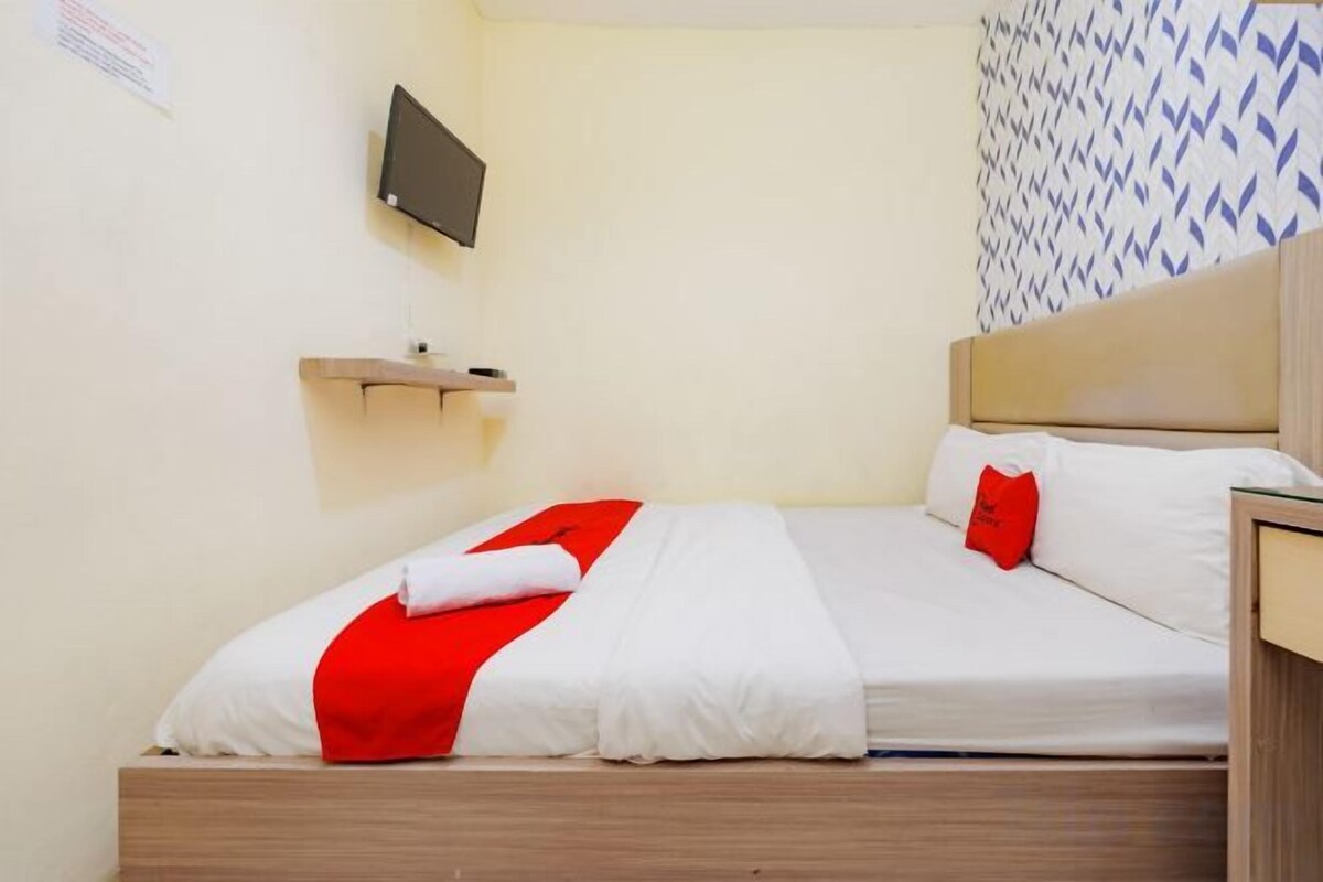 A single bed with a wooden headboard, a flat-screen TV mounted on the wall, and a patterned wall design.