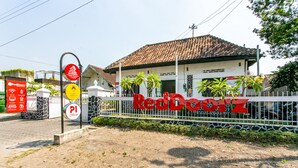 Entrada de un hotel RedDoorez con techo de tejas, cerca viva blanca y palmeras.