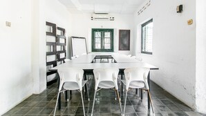 Un salón de conferencias con una mesa larga, sillas blancas, un ventanal verde y un techo blanco con un diseño floral.