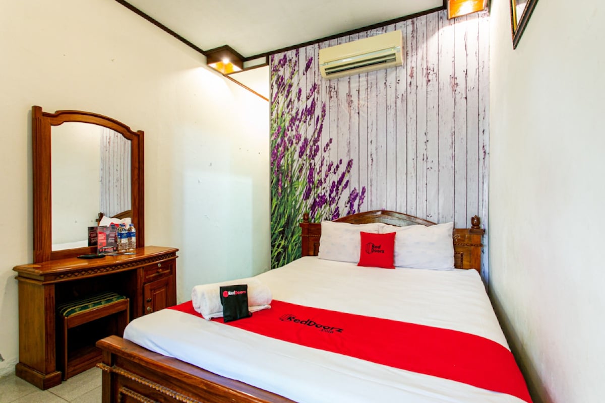 Une chambre d’hôtel avec un lit en bois, une table de chevet, un miroir et un climatiseur fixé au mur.