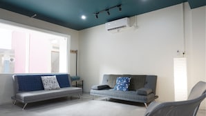 A modern living room with two grey sofas, one with a blue and white patterned pillow and the other with a floral pillow. An air conditioning unit is mounted on the wall above the sofas. - Residences by RedDoorz near MT Haryono (Jakarta)