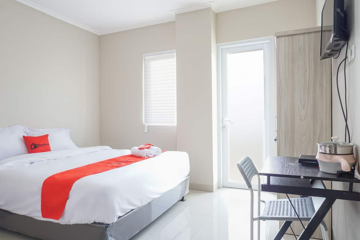 A hotel room with a bed, a table with a kettle, and a chair.