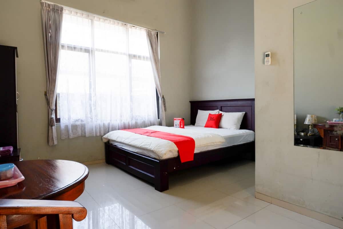 A bedroom with a bed, a bedside table, a window with curtains, and a wall-mounted phone.