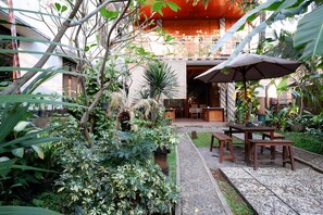 A courtyard with a wooden table and benches, surrounded by lush greenery and potted plants. - RedDoorz Syariah near Menara Kudus (Kudus)