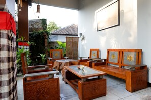 A traditional wooden furniture set with intricate carvings, a tiled floor, and a view of a garden with a tiled roof structure. - RedDoorz Syariah near Menara Kudus (Kudus)