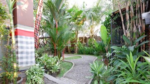 Un jardin avec un chemin pavé de pierres, des plantes en pot et une clôture en bambou.