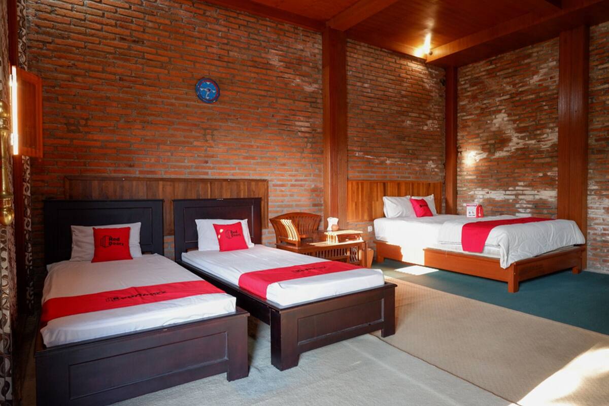 A hotel room with three beds, wooden headboards, and a brick wall.