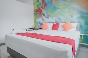Una habitación de hotel con cama, ropa de cama blanca, un plaid rojo y almohadas naranjas.