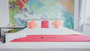 A hotel room with a bed, a red blanket, and a colorful abstract wall art.